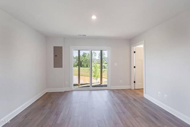 empty room featuring wood finished floors, visible vents, baseboards, and electric panel