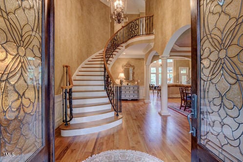 foyer featuring crown molding, ornate columns, wood finished floors, stairway, and arched walkways