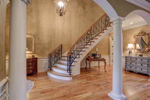 staircase with ornate columns, arched walkways, wood finished floors, and wainscoting