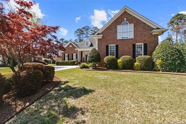 traditional-style house featuring a front lawn, driveway, an attached garage, and brick siding