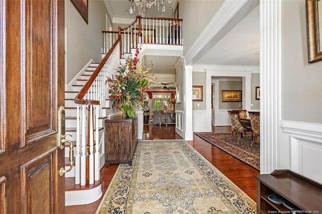 entrance foyer with a decorative wall, a chandelier, crown molding, stairway, and dark wood-type flooring