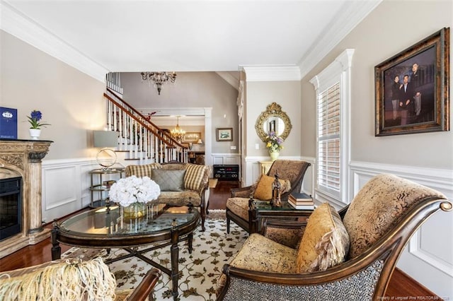 living area featuring crown molding, wood finished floors, wainscoting, a high end fireplace, and an inviting chandelier