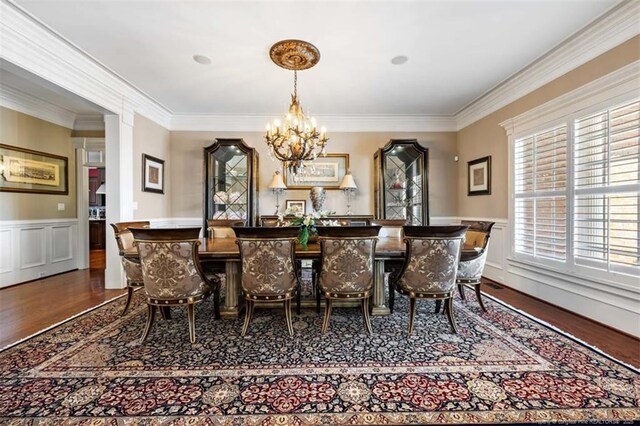 dining space with wood finished floors, indoor bar, crown molding, a chandelier, and wainscoting