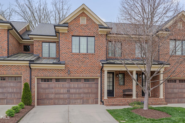 view of property with an attached garage, brick siding, a standing seam roof, and concrete driveway