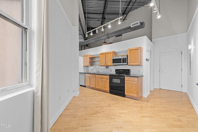 kitchen with track lighting, appliances with stainless steel finishes, a towering ceiling, and light wood finished floors