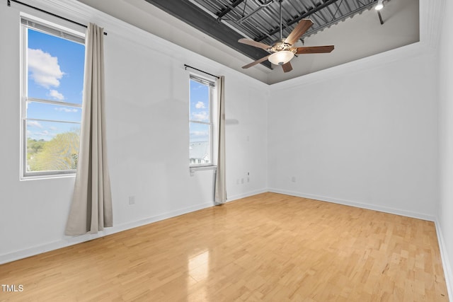 empty room featuring a tray ceiling, baseboards, a ceiling fan, and wood finished floors