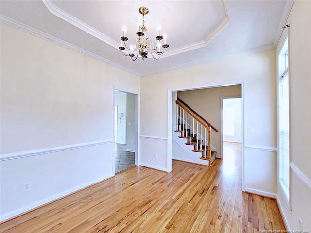 spare room with stairs, a notable chandelier, a raised ceiling, wood finished floors, and ornamental molding