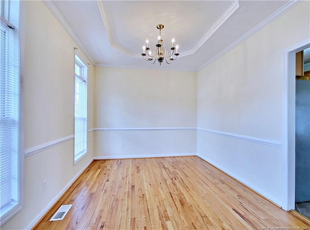 empty room featuring a raised ceiling, a healthy amount of sunlight, a chandelier, and wood finished floors