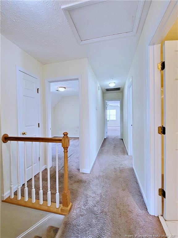 hall with attic access, carpet, baseboards, a textured ceiling, and visible vents