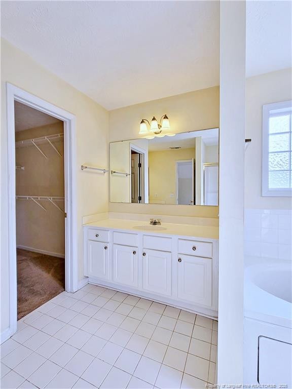 bathroom with tile patterned flooring, a bathtub, a walk in closet, and vanity