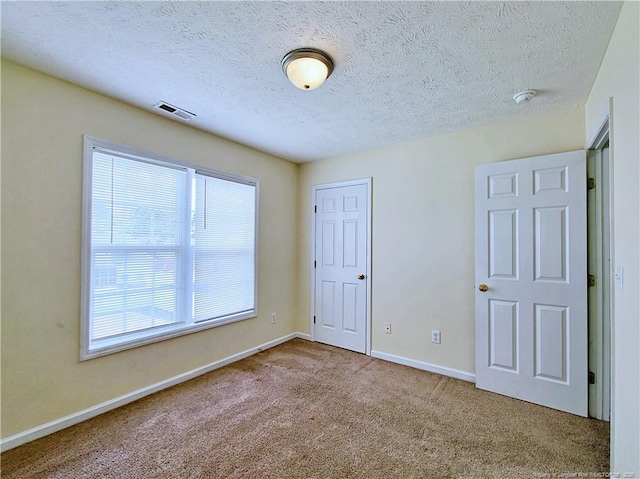 unfurnished bedroom with carpet flooring, a textured ceiling, baseboards, and visible vents