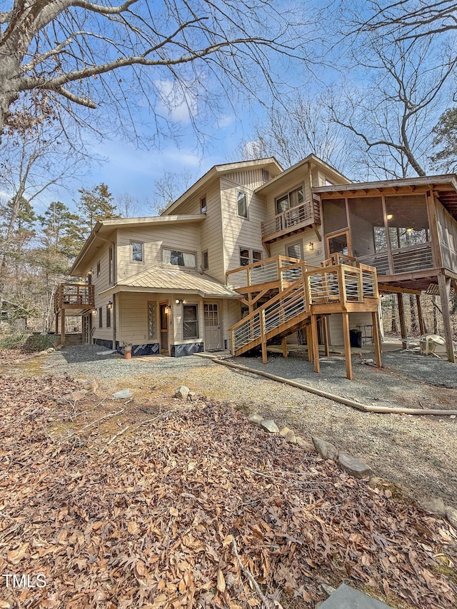 rear view of property featuring a sunroom, a balcony, a wooden deck, and stairway