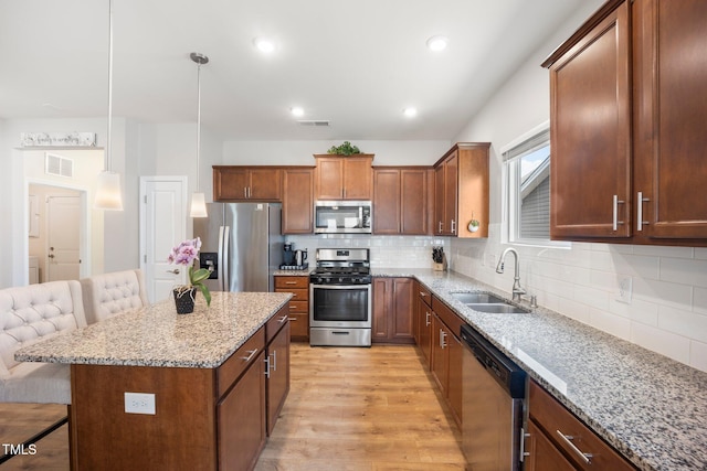 kitchen with stainless steel appliances, a sink, a kitchen breakfast bar, light wood-type flooring, and light stone countertops