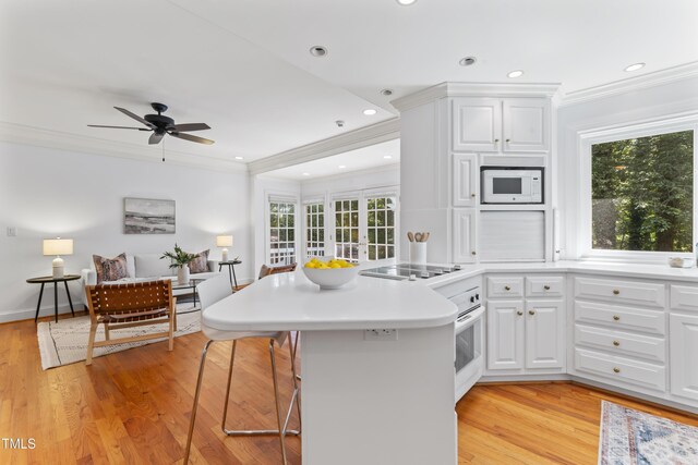 3911 Hope Valley Rd, Durham, NC 27707 - kitchen with a peninsula, crown molding, light wood-type flooring, a kitchen breakfast bar, and white cabinets