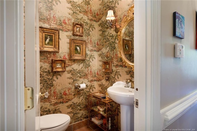 half bath with baseboards, wallpapered walls, and toilet