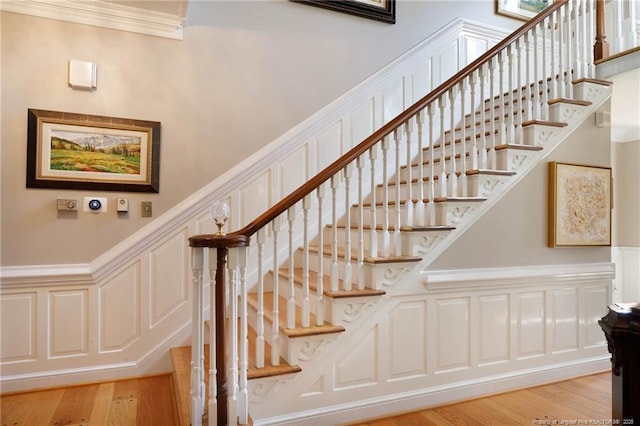 stairs with a wainscoted wall, crown molding, wood finished floors, and a decorative wall