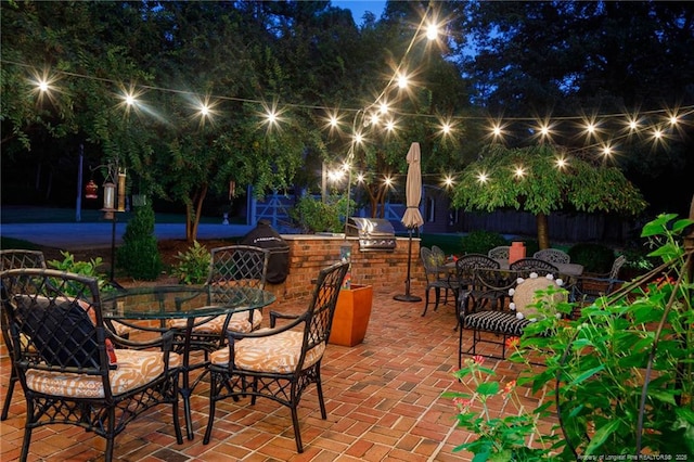 patio at night with grilling area, fence, outdoor dining space, and area for grilling