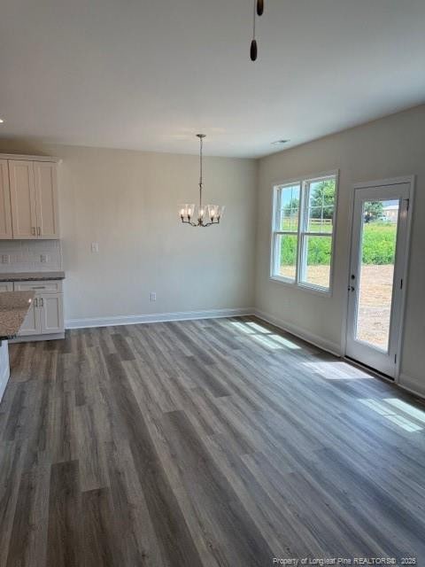 unfurnished dining area featuring a chandelier, baseboards, and dark wood-style floors