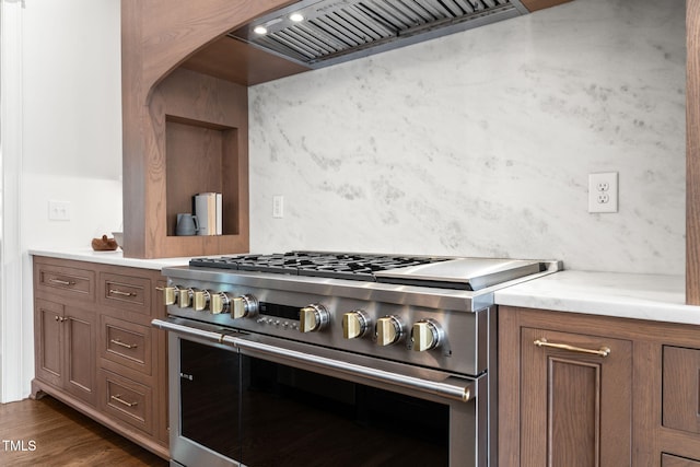 kitchen with brown cabinetry, dark wood-style flooring, stainless steel stove, light countertops, and premium range hood