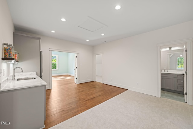 unfurnished living room featuring a sink, light wood-style flooring, attic access, recessed lighting, and baseboards
