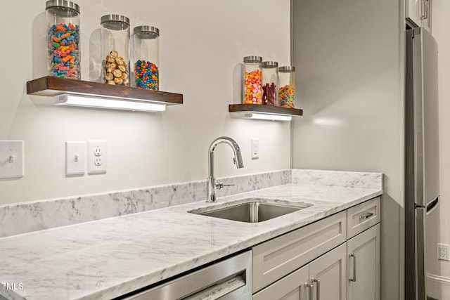 kitchen featuring open shelves, freestanding refrigerator, dishwashing machine, light stone counters, and a sink