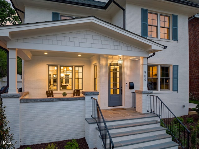 doorway to property featuring a porch and brick siding