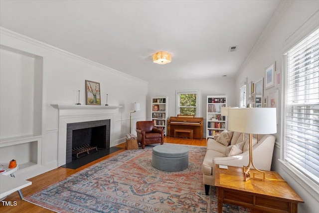 living area with a fireplace with flush hearth, wood finished floors, ornamental molding, and visible vents