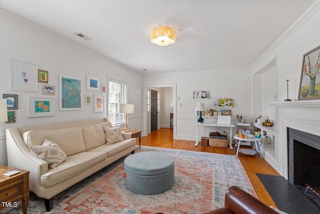 living area with a fireplace with flush hearth, crown molding, wood finished floors, and visible vents
