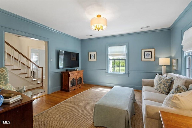 living area with crown molding, wood finished floors, visible vents, and stairs