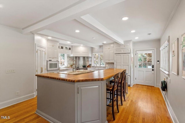 kitchen with tasteful backsplash, wood counters, white cabinets, beam ceiling, and light wood finished floors
