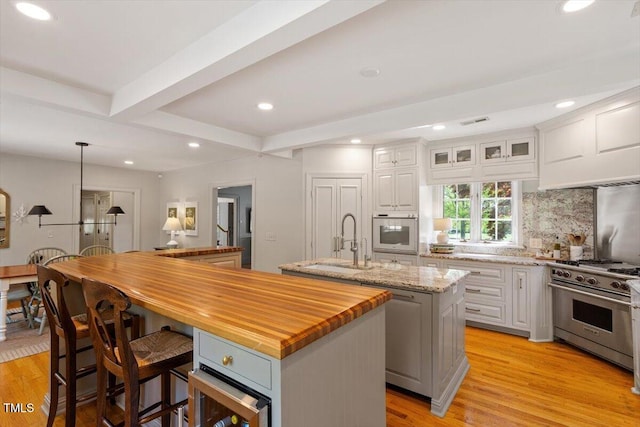 kitchen featuring light wood-style floors, an island with sink, white oven, premium range, and butcher block countertops