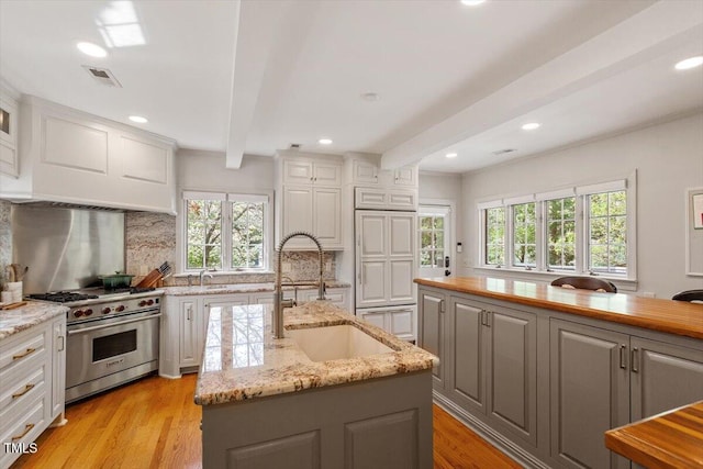 kitchen featuring luxury stove, beam ceiling, gray cabinetry, and visible vents