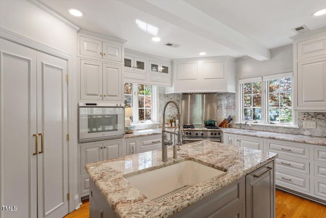 kitchen with high end stainless steel range oven, tasteful backsplash, beamed ceiling, oven, and a sink