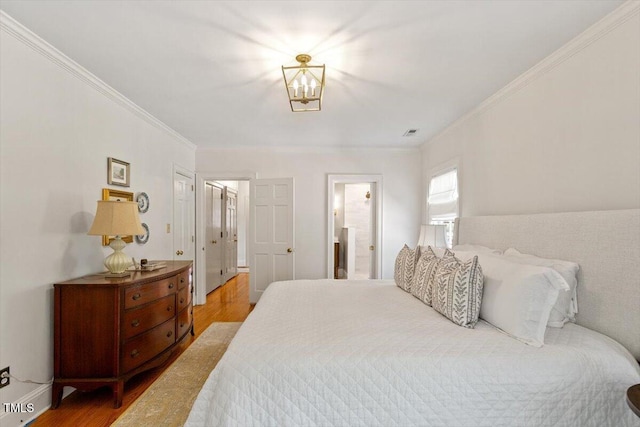 bedroom with baseboards, a chandelier, crown molding, visible vents, and wood finished floors