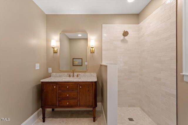bathroom with baseboards, tiled shower, and vanity