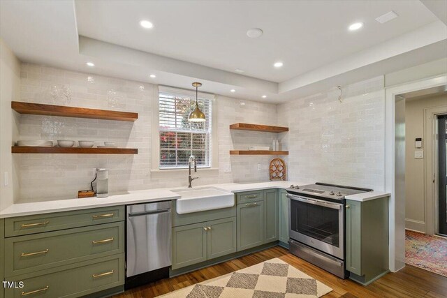 kitchen with green cabinets, open shelves, appliances with stainless steel finishes, light countertops, and a sink