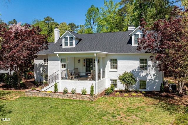 view of front of home with a front yard, roof with shingles, covered porch, and a chimney