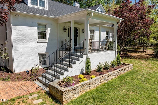 view of front of property with brick siding, a front yard, a porch, and roof with shingles
