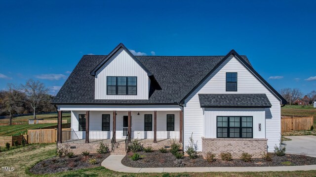modern farmhouse style home with fence, brick siding, board and batten siding, roof with shingles, and a porch