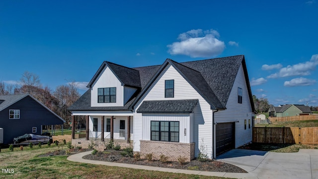 modern inspired farmhouse featuring fence, an attached garage, brick siding, driveway, and covered porch