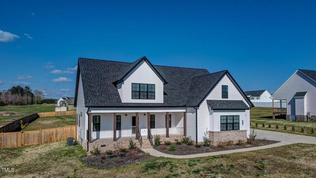 modern farmhouse style home featuring covered porch, a shingled roof, fence, and a front lawn