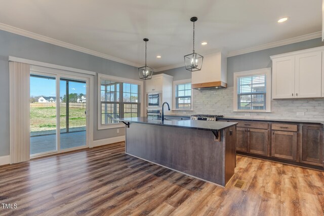 kitchen featuring custom range hood, range, a sink, dark countertops, and light wood-style floors