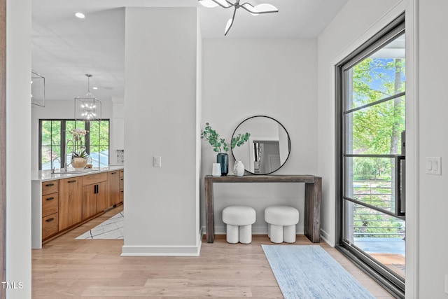 interior space with baseboards, an inviting chandelier, plenty of natural light, and light wood-style flooring