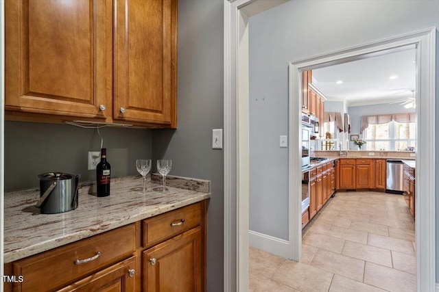 1525 Marshall Farm St, Wake Forest, NC 27587 - kitchen featuring light tile patterned flooring, light stone countertops, appliances with stainless steel finishes, brown cabinets, and baseboards