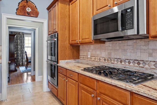 1525 Marshall Farm St, Wake Forest, NC 27587 - kitchen with brown cabinets, light stone counters, backsplash, and appliances with stainless steel finishes