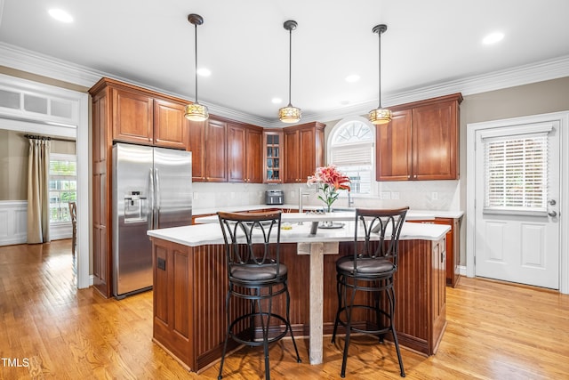 3821 Falls River Ave, Raleigh, NC 27614 - kitchen featuring stainless steel fridge with ice dispenser, a center island, light countertops, light wood-type flooring, and ornamental molding