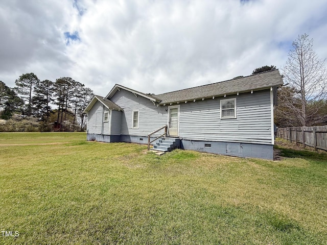 rear view of property with fence, a lawn, a shingled roof, entry steps, and crawl space