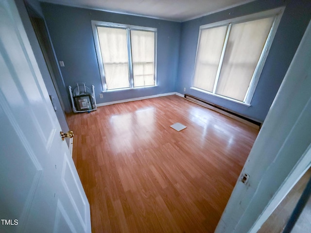 unfurnished room featuring baseboards, baseboard heating, and wood finished floors