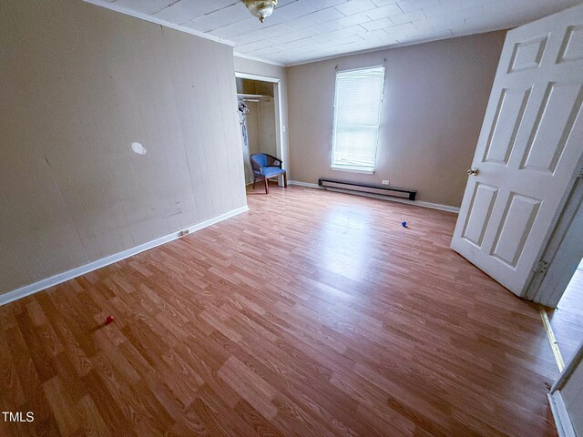 unfurnished bedroom featuring baseboards, wood finished floors, a baseboard heating unit, and ornamental molding