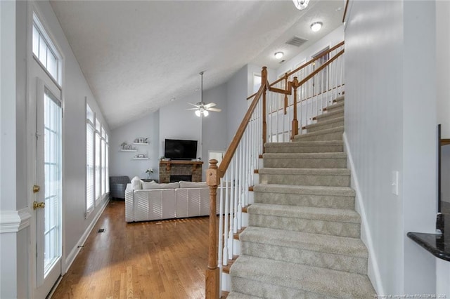 6826 Surrey Rd, Fayetteville, NC 28306 - stairway with high vaulted ceiling, ceiling fan, visible vents, a fireplace, and wood finished floors